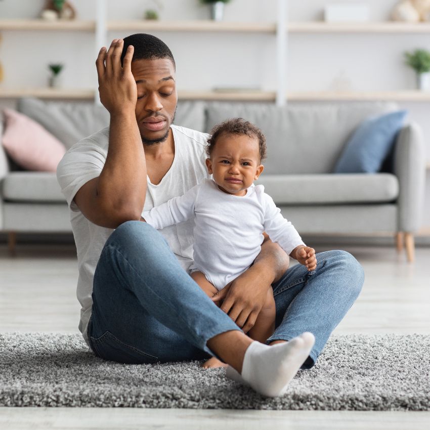 Black father with crying baby looking stressed