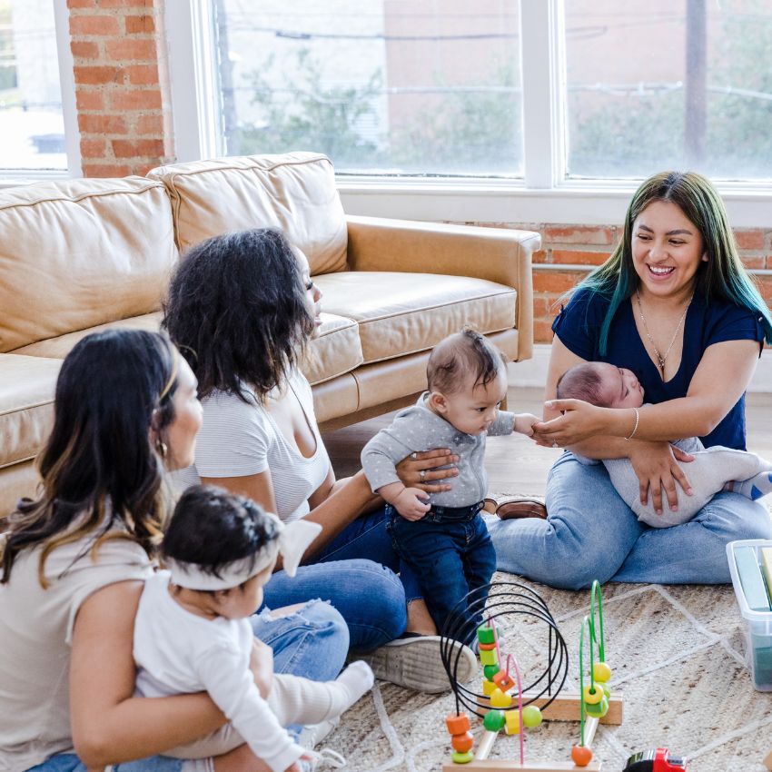 Group of 3 women each with a baby sitting on the floor with baby toys