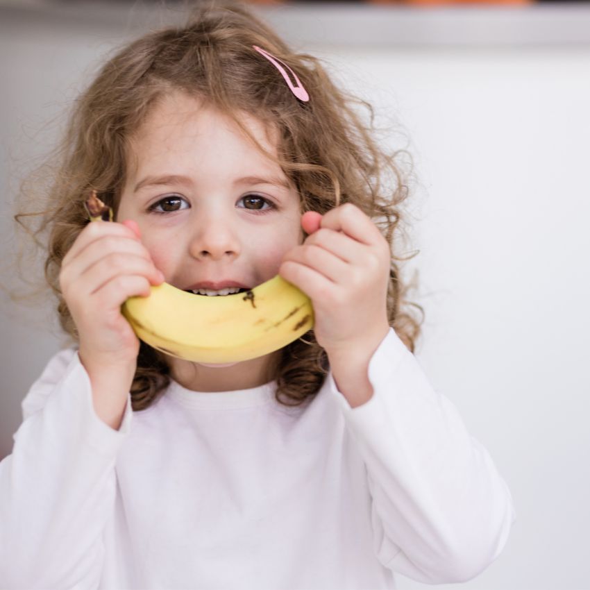 Curly haired white girl holding a banana to her face