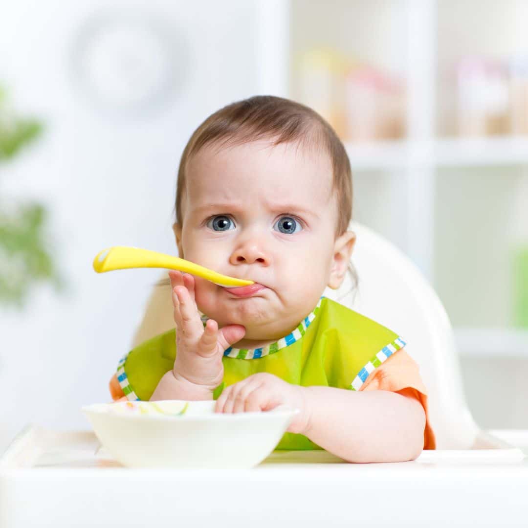Baby in highchair with weaning spoon and bowl