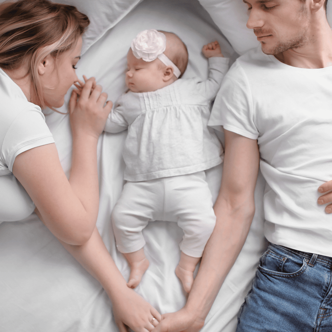Female and male laying either side of a baby in bed sleeping